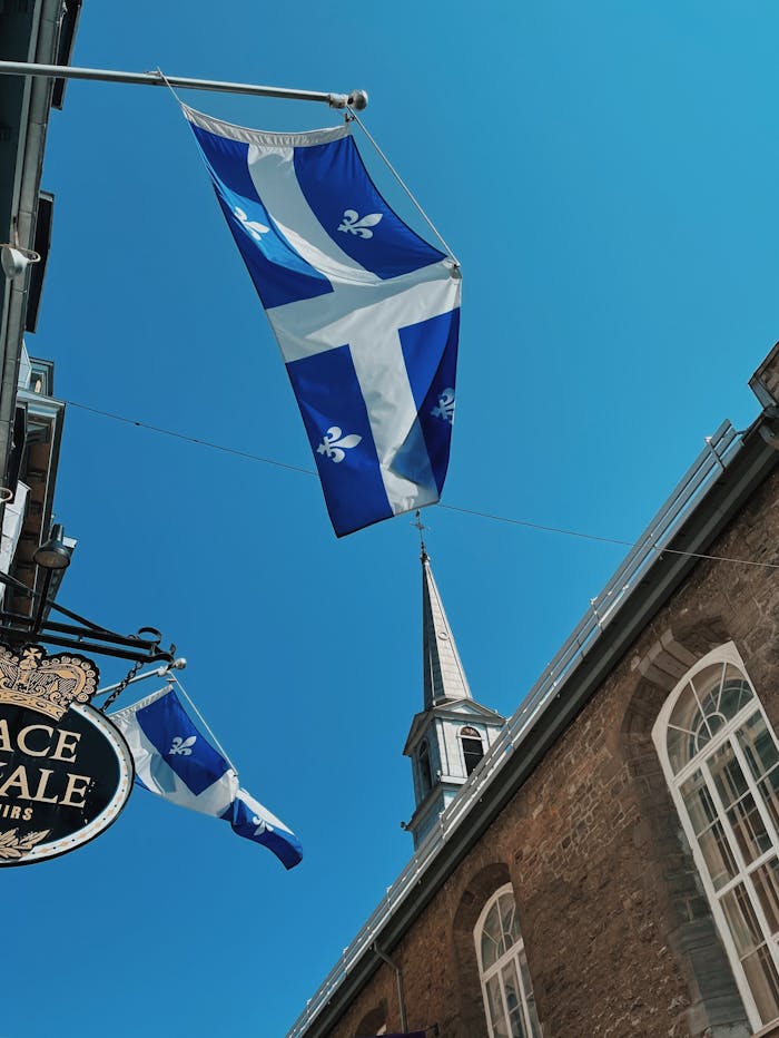 zipwp-image-12306710 Flag of Quebec on Pole Hanging from a Building Under Blue Sky